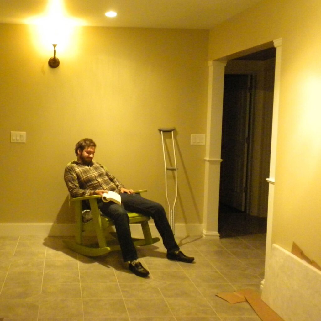 my bearded brother reading in a rocking chair indoors amongst an empty yellow room